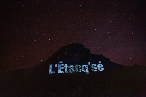 An image of a large stack with the Jèrriais name for this place in large letters, projected onto the rock.