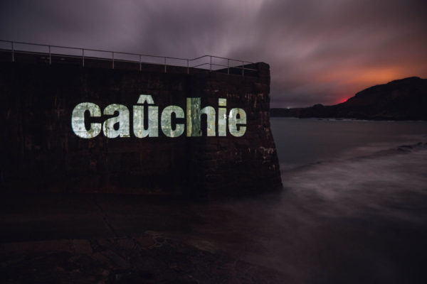 An image of a pier with the Jèrriais word for pier in large letters, projected onto the pier wall.
