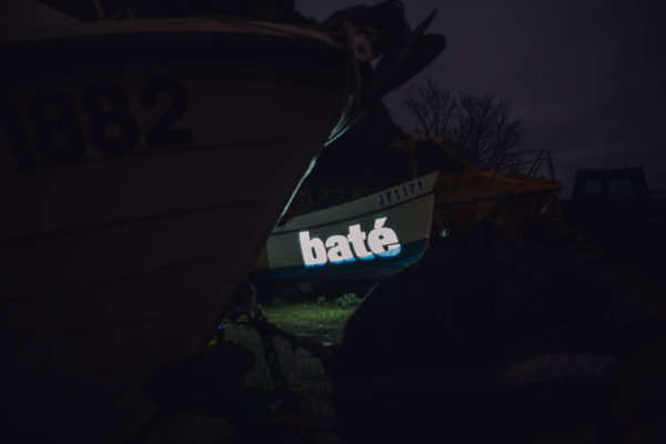 An image of an boat with the Jèrriais word for boat in large letters, projected onto the hull.