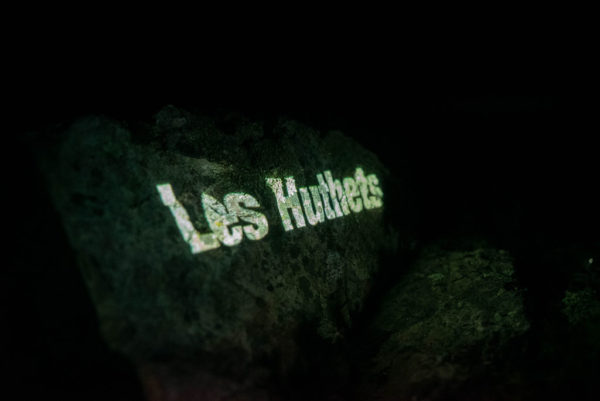 An image of an Les Hurets headland with the Jèrriais word for Les Hurets in large letters, projected onto the headland.