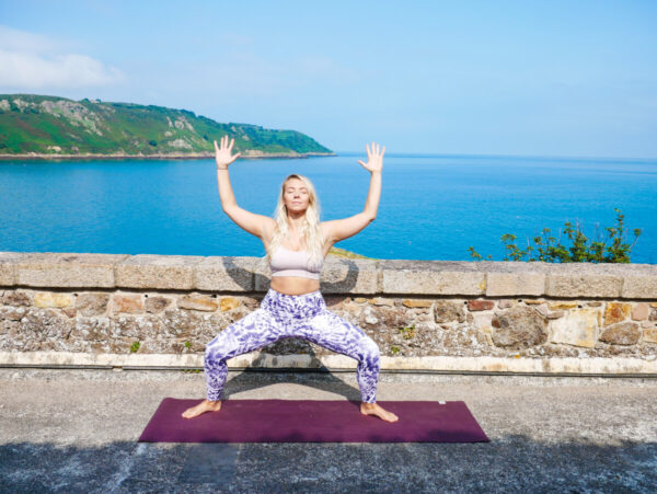 woman does yoga pose with the sea in the background
