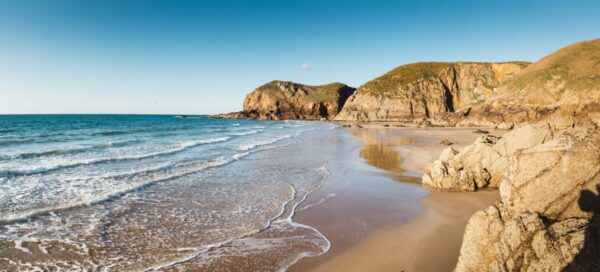 Plemont Bay. granite cliffs and a sandy beach with waves lapping the shore.