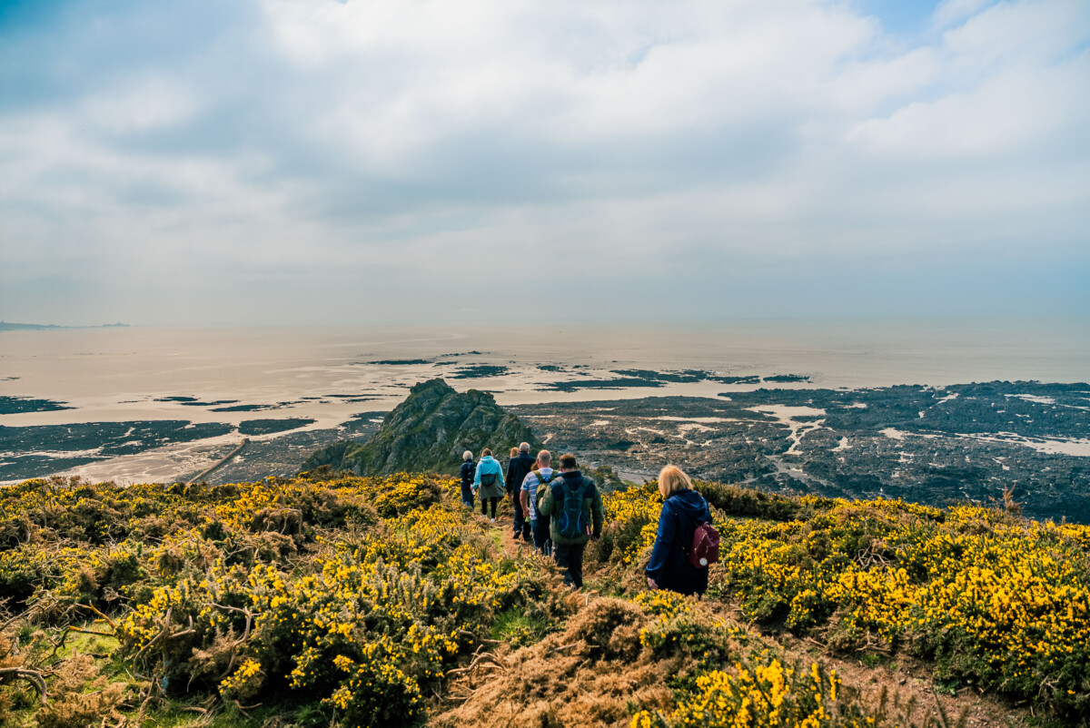 Landscape colour photograph of a group of walkers on a cliff top at low tide.